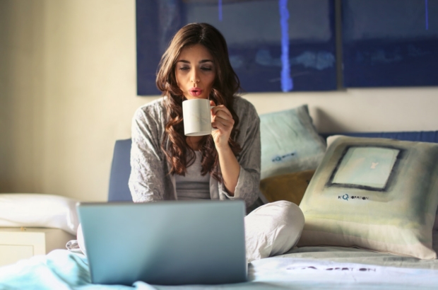 woman-in-grey-jacket-sits-on-bed-uses-grey-laptop-935743